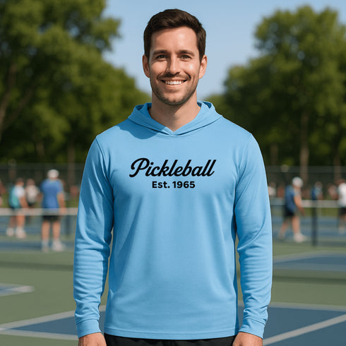 Man wearing a blue hoodie with 'Pickleball Est. 1965' text on a pickleball court.